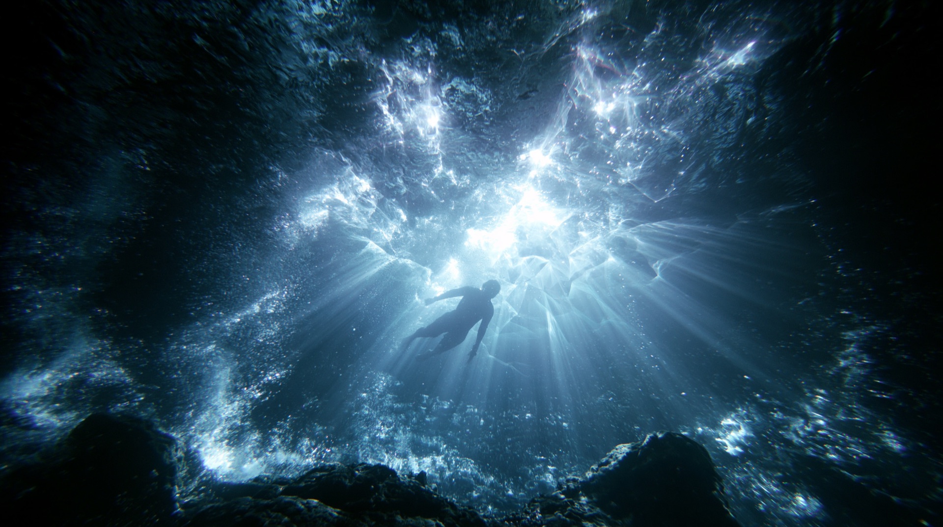 A diver silhouetted in light beneath the surface of the pool