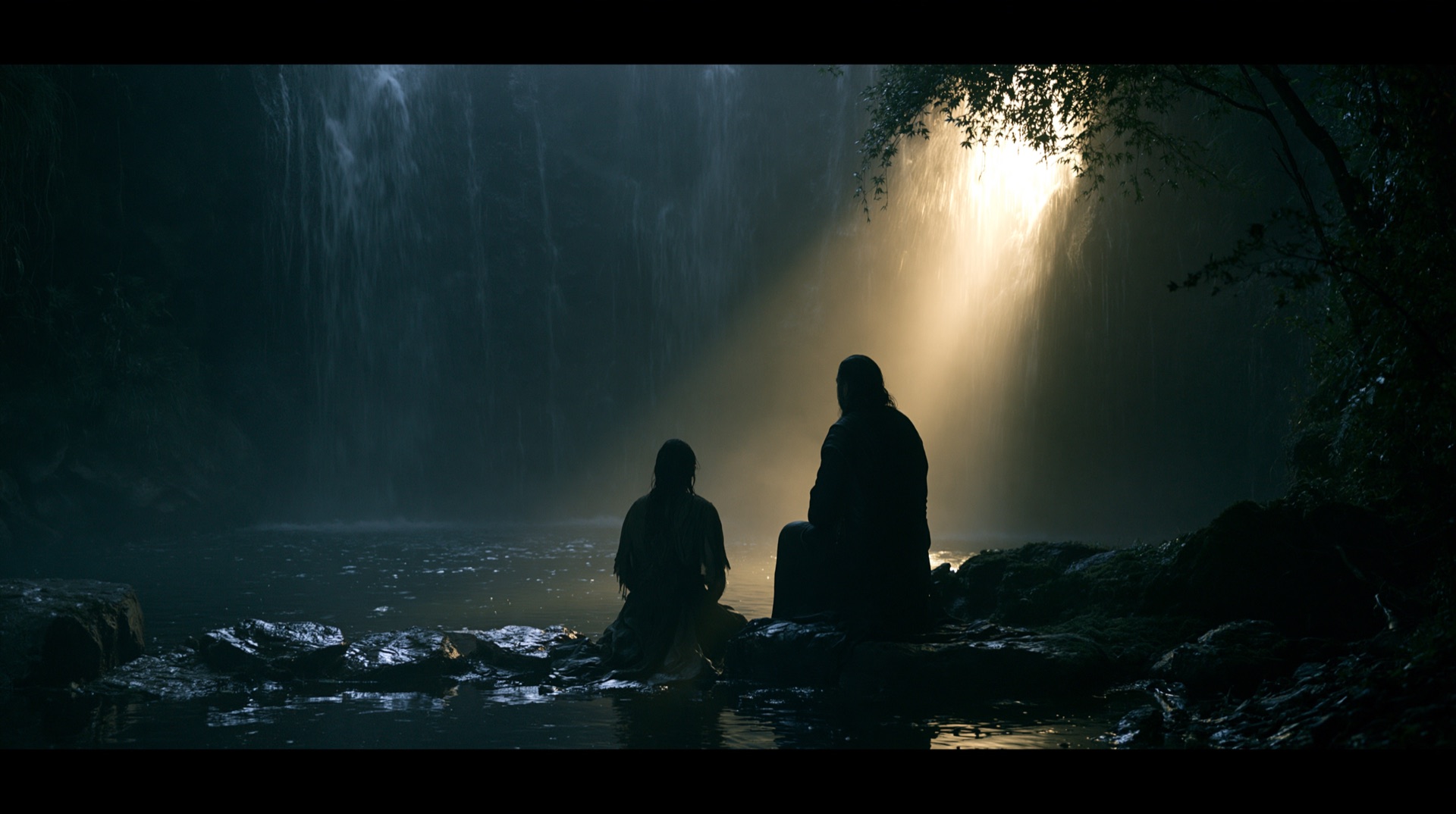Two figures at the edge of the waterfall pool in a shaft of light